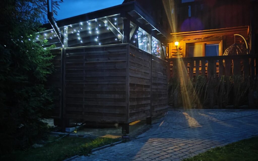 Duży domek wieczorem, przed nim obudowana strefa z jacuzzi